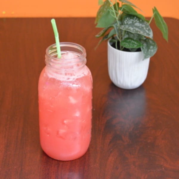 Pink drink in a mason jar with a green straw, next to a potted plant on a wooden table.