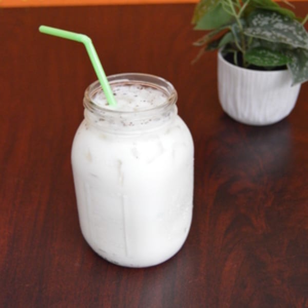 A refreshing horchata in a mason jar with a green straw, next to a small potted plant.